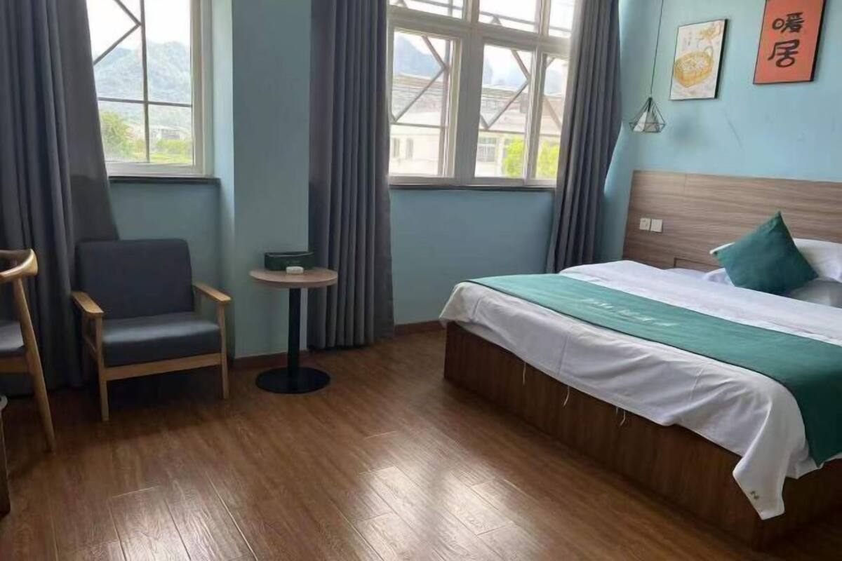 Une chambre d’hôtel avec un lit, une chaise, une petite table et une fenêtre avec des rideaux.