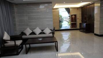 A modern hotel lobby with a sofa, chairs, a coffee table, and a television.