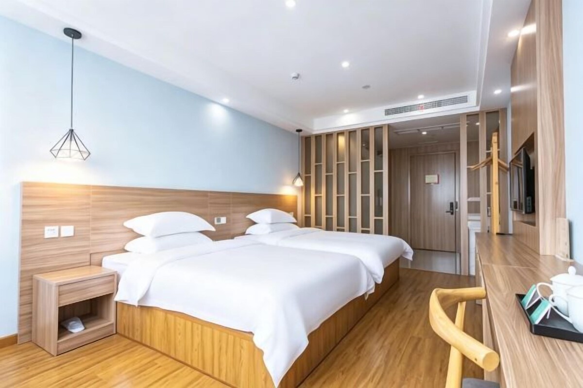 Ein Hotelzimmer mit hölzernem Kopfteil, zwei Betten, einem kleinen Nachttisch, einem Sessel und einem Schreibtisch mit Spiegel und Tasse.