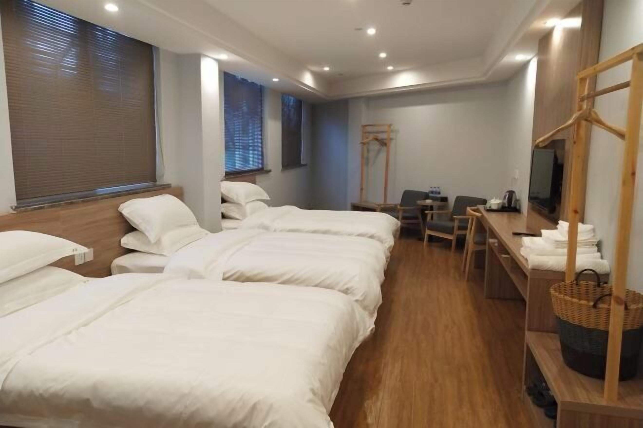 A hotel room with three beds, a desk, a chair, a television, and a wooden wardrobe.