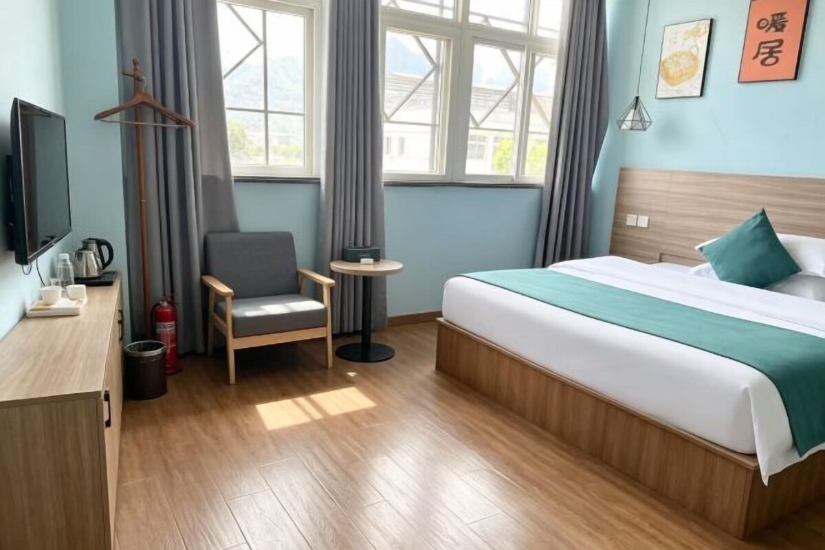 Ein Hotelzimmer mit einem Bett, einem Sessel, einem kleinen Tisch, einem Fernseher und einem Fenster mit Vorhängen.