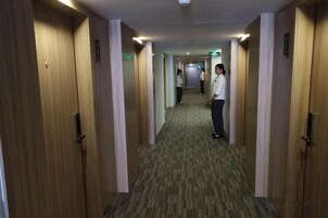 Un pasillo de hotel con puertas de madera, piso alfombrado y una persona parada a lo lejos.