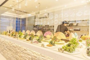 Un restaurant amb una barra llarga, diferents plats i un cuiner preparant aliments.