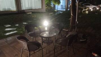 Zona exterior amb una taula rodona i cadires, un arbre i un cotxe al fons.