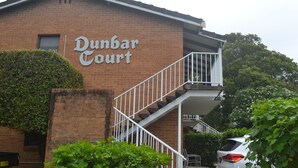 A building with a sign reading "Dunbar Court." It features a brick facade, a white staircase, and a small balcony. - Dunbar Court Unit 8 - South West Rocks (SOUTH WEST ROCKS)