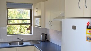 A kitchen with white cabinets, a stainless steel sink, a kettle, and a refrigerator with an energy rating sticker. - Dunbar Court Unit 8 - South West Rocks (SOUTH WEST ROCKS)