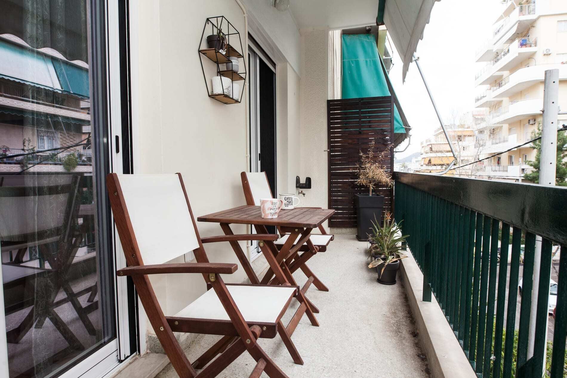 Een balkon met houten stoelen en een tafel, een plant in pot en een metalen plank met spullen.