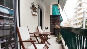 A balcony with wooden chairs and a table, a potted plant, and a metal shelf with items.