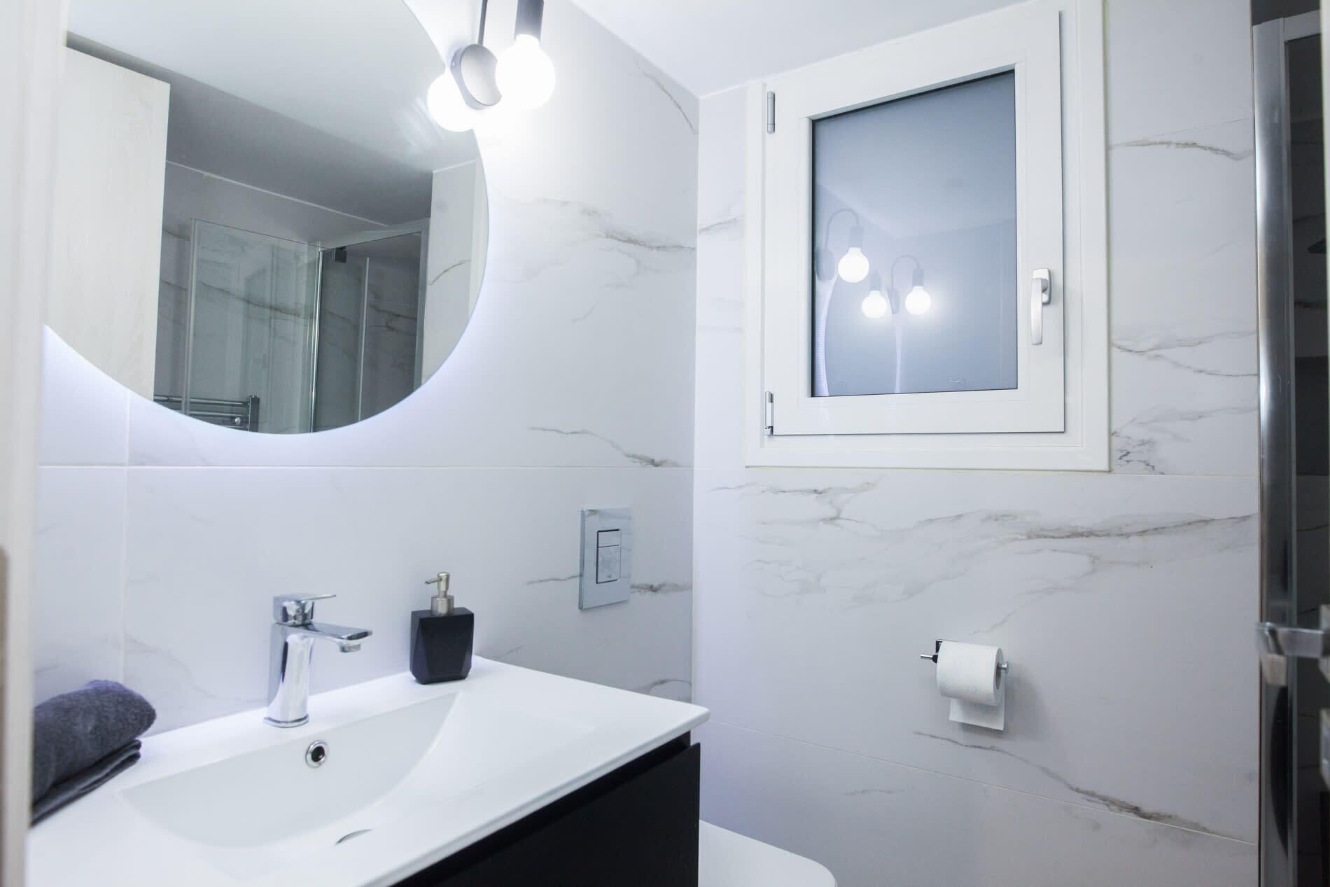 Une salle de bain moderne avec un lavabo blanc, un miroir et une douche à parois de verre.