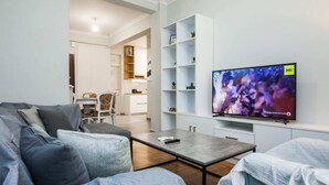 A modern living room with a flat-screen TV, a sofa, a coffee table, and a dining area with chairs and a small table.