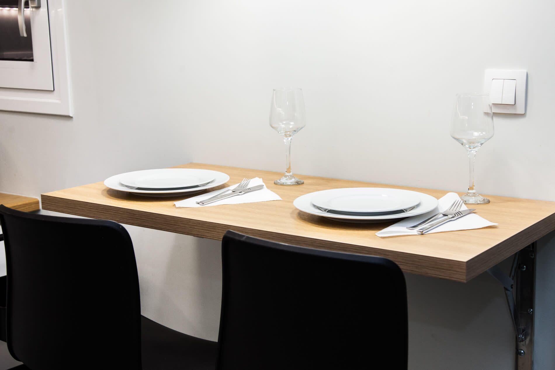 A dining table set with plates, cutlery, and wine glasses, flanked by black chairs.