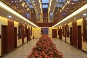 A hotel corridor with a central floral arrangement, wooden doors, and a modern ceiling design.