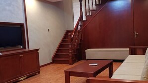 A living room with a wooden staircase, a sofa, a coffee table, and a TV on a cabinet. - Guihou Hotel (Kunming)