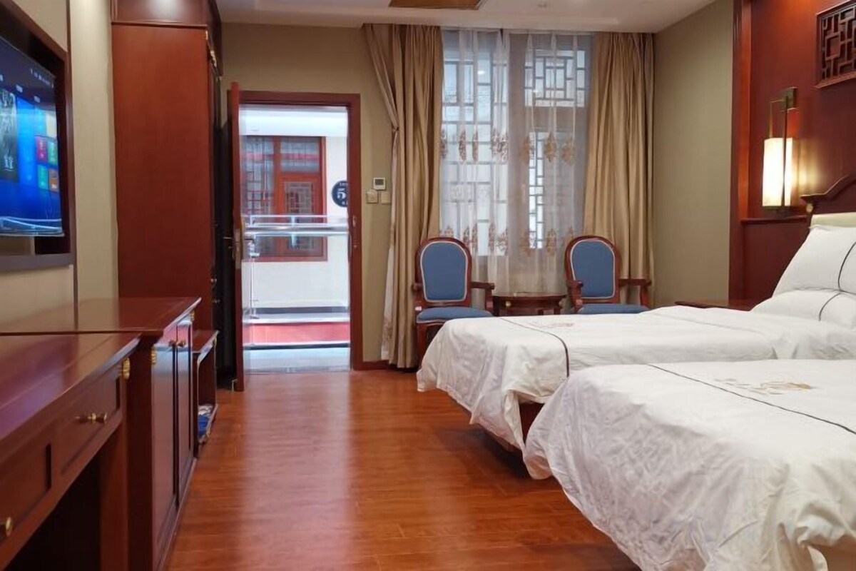 A hotel room with a TV, two beds, a desk, and a chair.