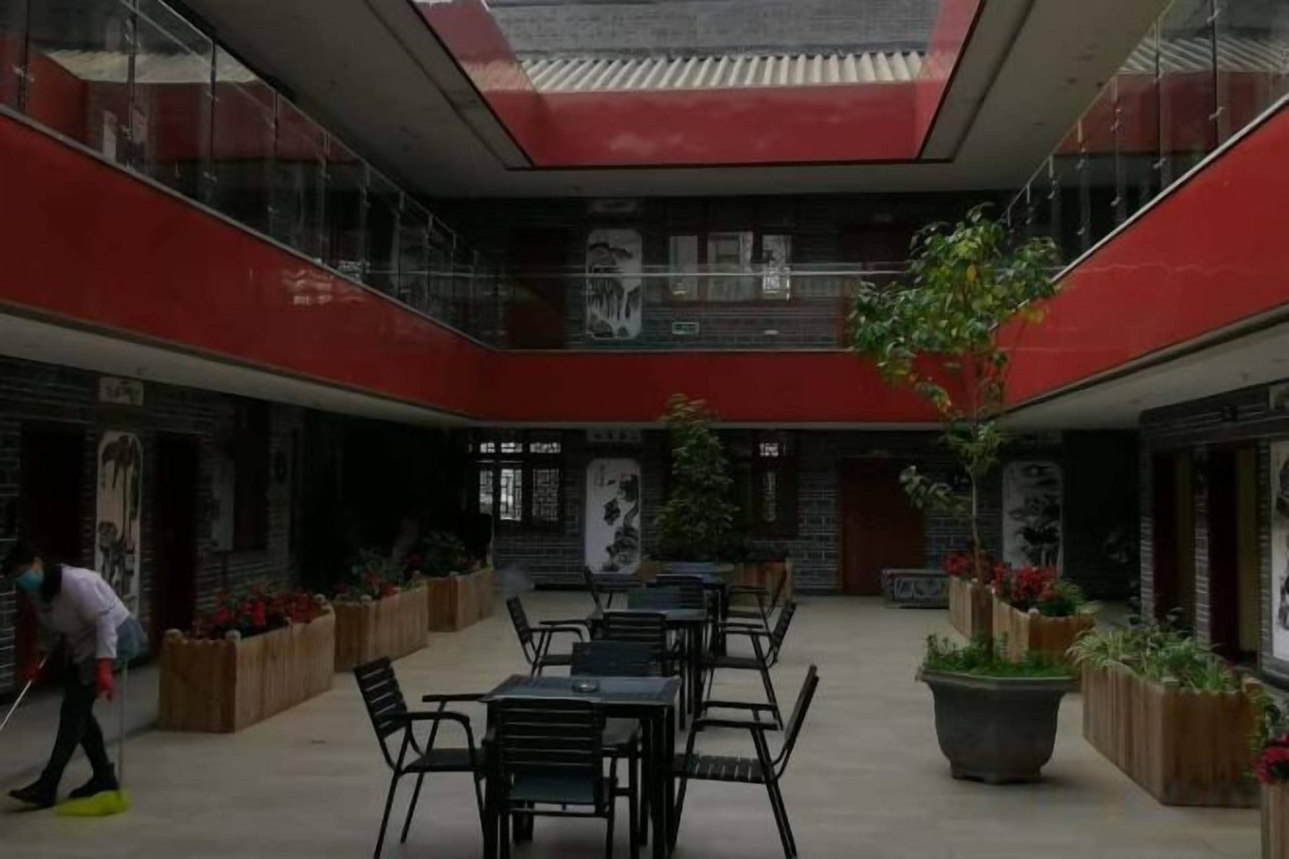 Un espacio interior amplio con varias mesas y sillas, una jardinera grande con plantas, y una persona limpiando.
