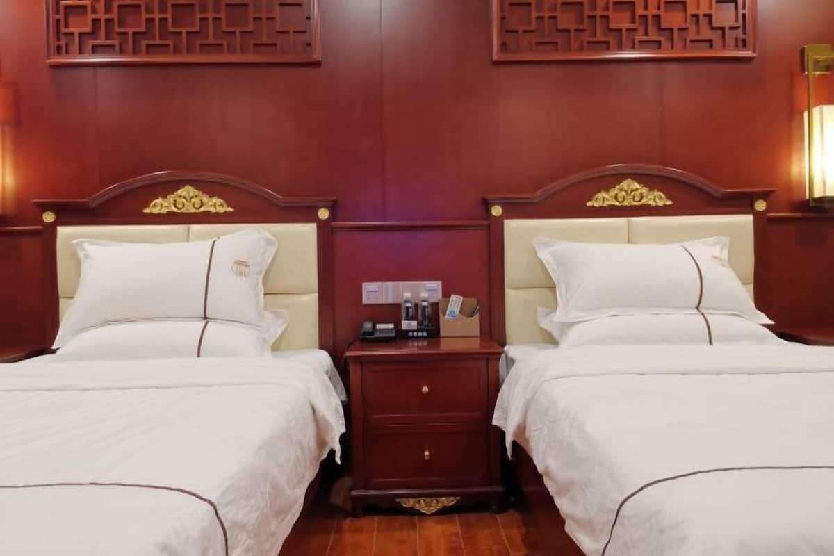 Quarto de hotel com duas camas, uma mesa de cabeceira de madeira com um telefone e uma pequena mesa, e um painel decorativo na parede.