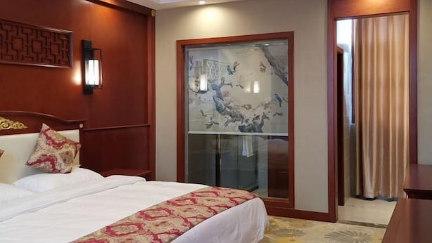A hotel room with a bed, a decorative wall panel, a window with a view, and a door with curtains. - Guihou Hotel (Kunming)