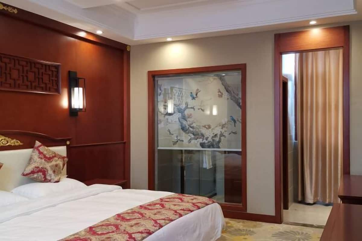 Quarto de hotel com cama, um painel decorativo na parede, janela com vista e porta com cortinas.