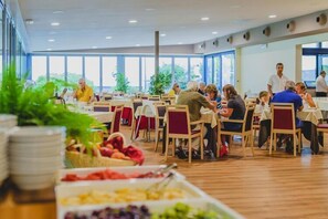Une cafétéria avec des tables et des chaises, où les gens prennent leurs repas, et où la nourriture est exposée.