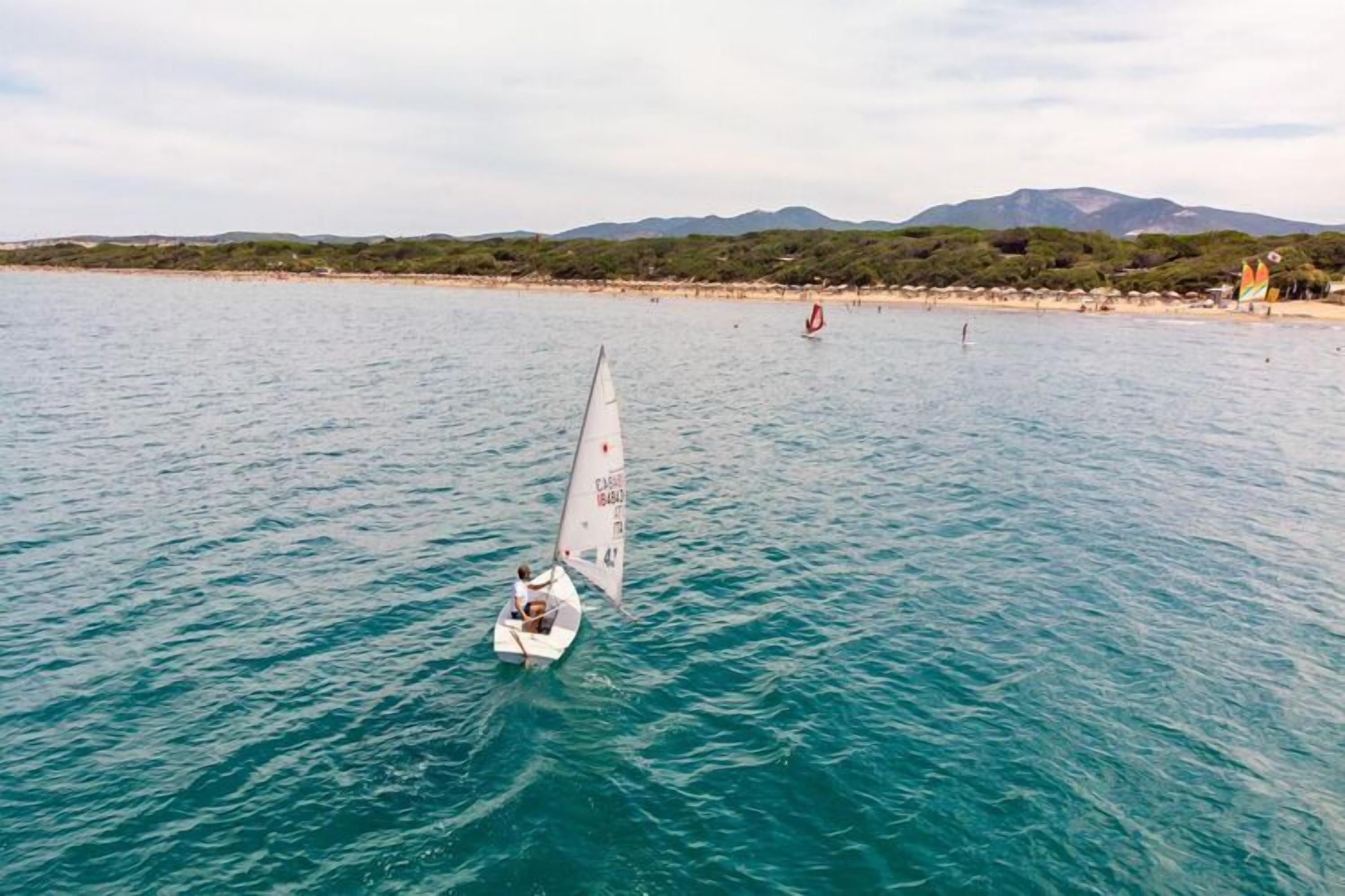 Un voilier sur une eau calme, avec une plage et des montagnes en arrière-plan.