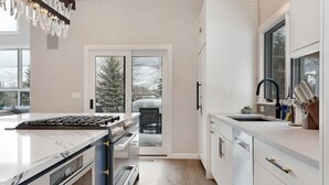 Een moderne keuken met een groot eiland, een ingebouwde oven en zicht op een besneeerd landschap door de schuifpui.