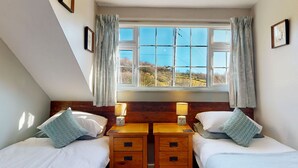 A bedroom with two beds, a window with a view of the countryside, and a wooden dresser between the beds.
