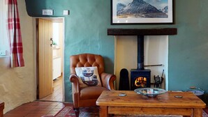 A cozy room with a leather armchair, a wooden table, a fireplace, and a framed landscape painting.
