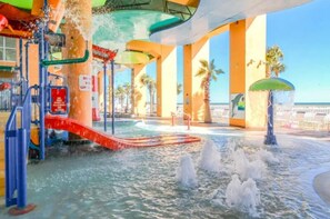 An indoor water park with slides, water jets, and palm trees.