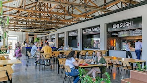 Um restaurante moderno com vigas de madeira aparentes, várias áreas de estar e um bar de sushi.