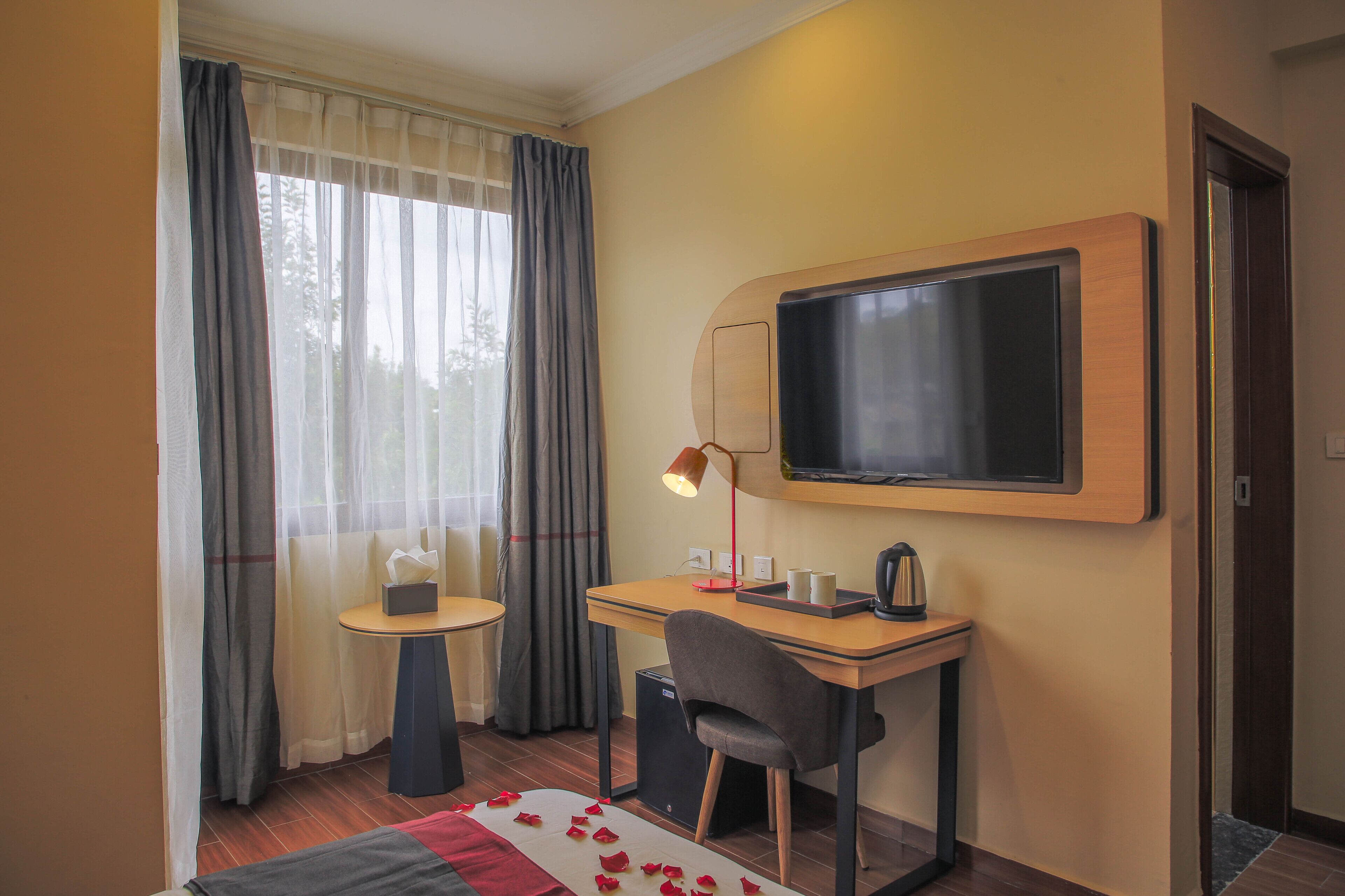 Een hotelkamer met een bureau, stoel, televisie en een bijzettafeltje met een lamp.