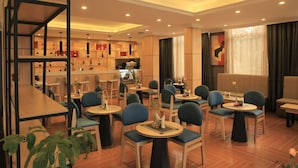 Un moderno vestíbulo de hotel con mesas redondas, sillas azules, suelo de madera y una zona de bar con estantes llenos de botellas.