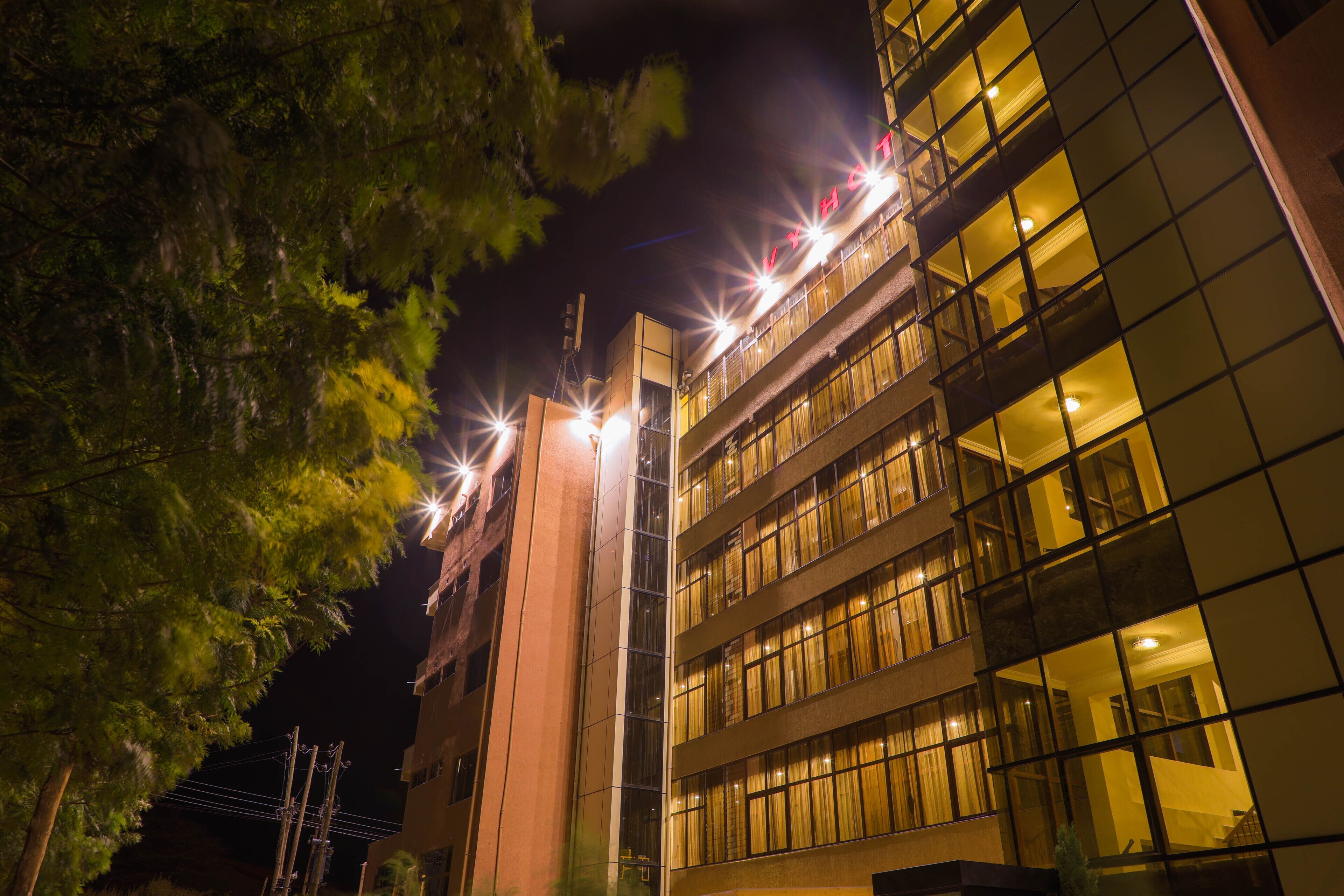 Um edifício com vários andares, janelas iluminadas e uma estrutura de linha de energia visível.