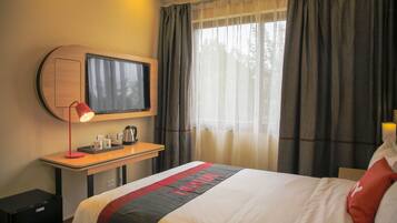 Een hotelkamer met een bed, een bureau met lamp, een televisie en een raam met gordijnen.