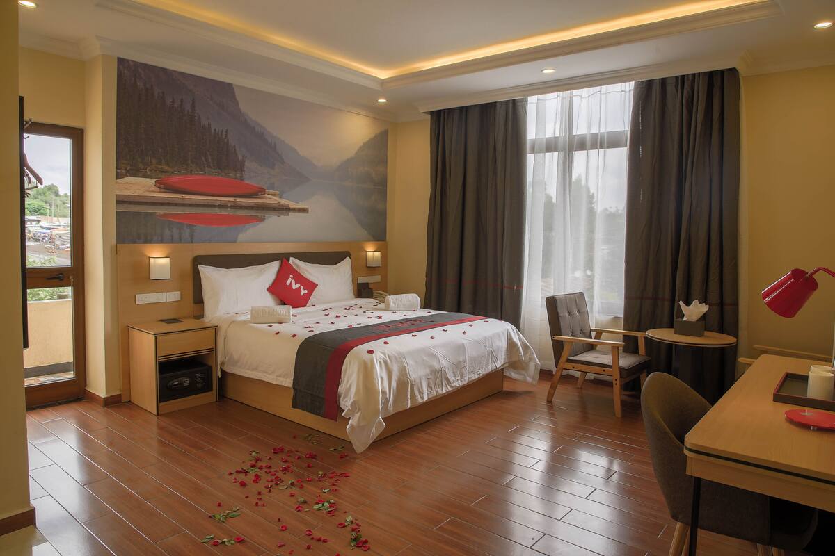 A hotel room with a large bed, a desk, a chair, a small table, and a window with curtains.