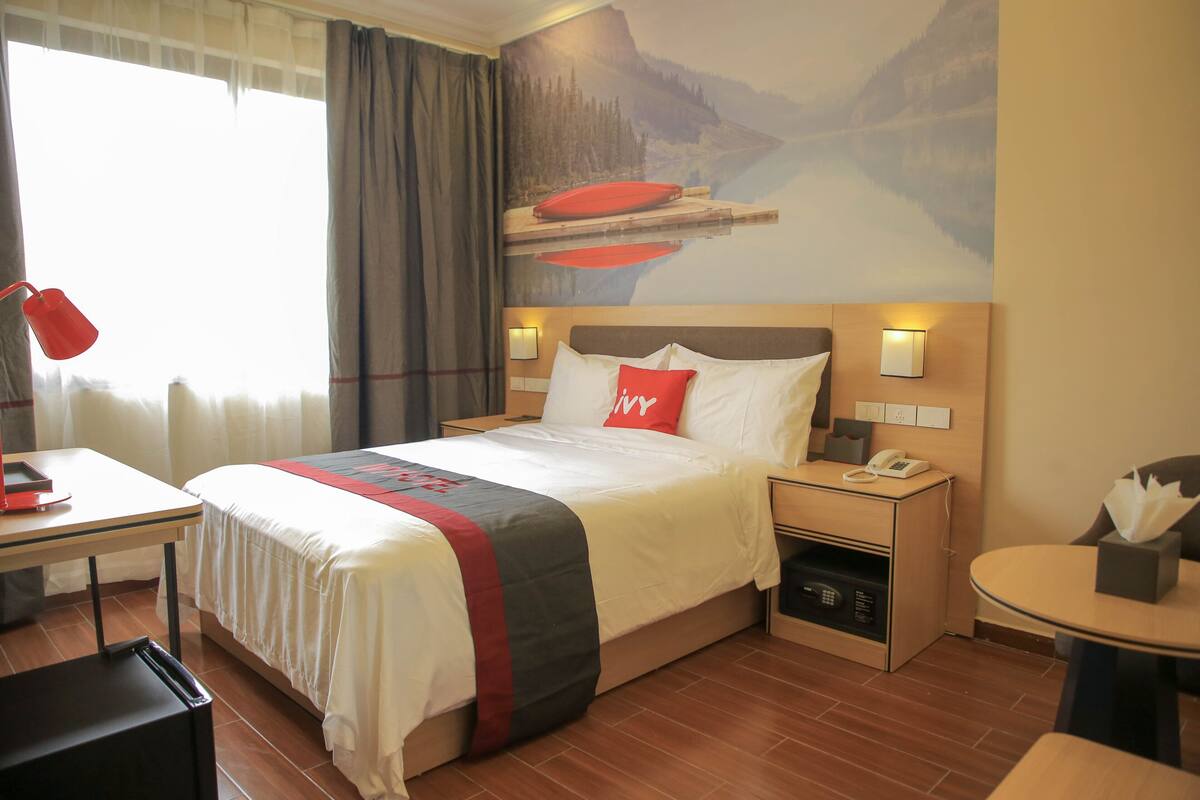 A hotel room with a bed, a desk, a chair, a nightstand, a phone, and a table with a tissue box.