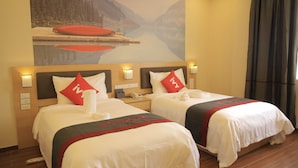 Habitación de hotel con dos camas, cada una con una almohada roja y una colcha blanca. En la pared sobre las camas, hay un cuadro de un lago y montañas.