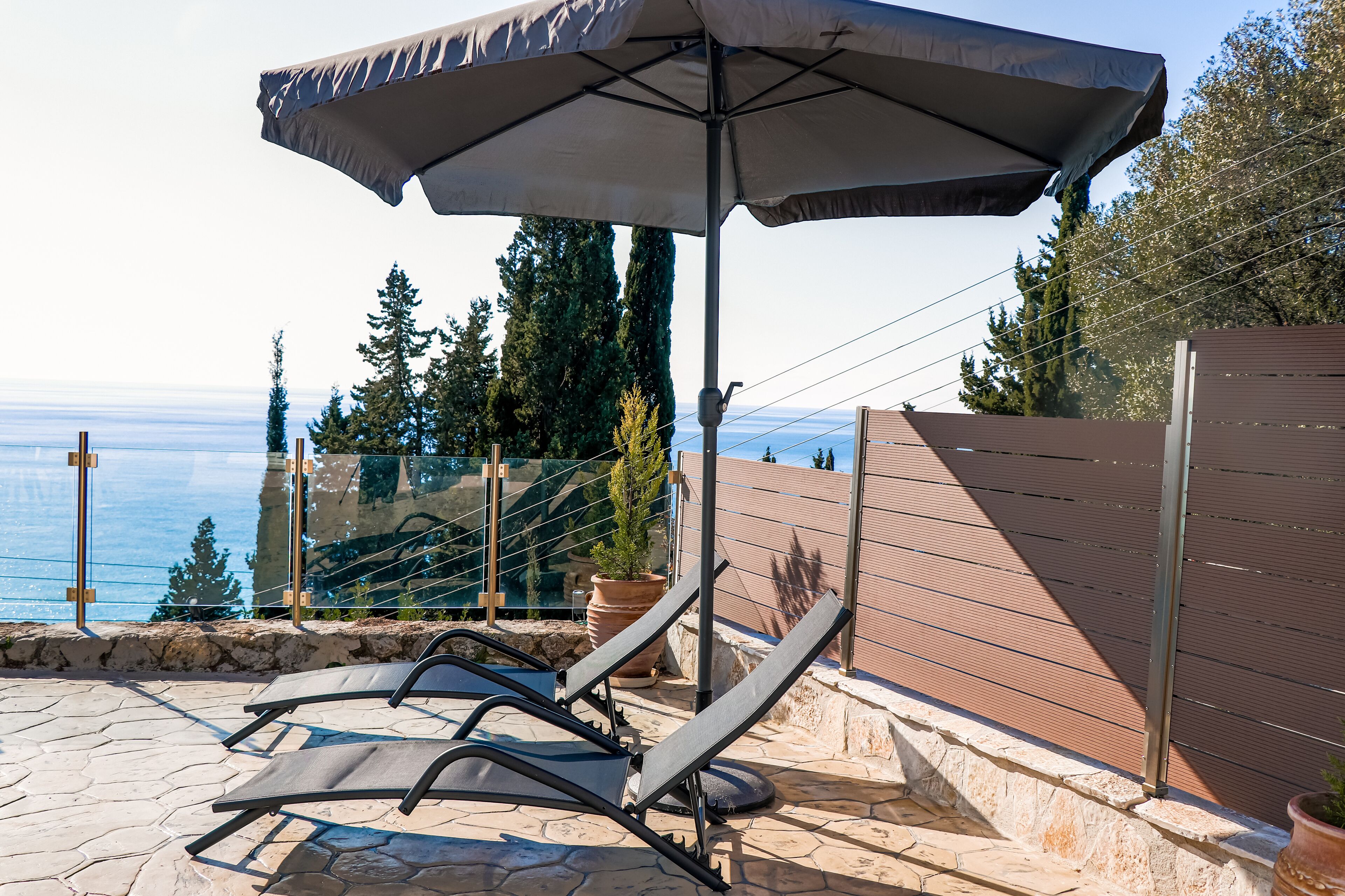 Un transat avec un grand parasol, une terrasse en pierre et une vue sur la mer.