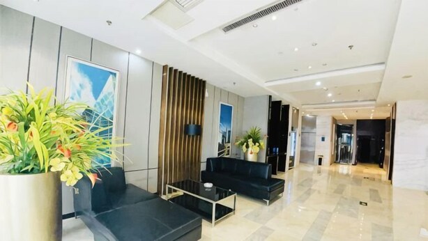 Eine moderne Lobby mit schwarzen Sofas, einem Couchtisch, einer großen Küstpflanze und einer Holzwand.