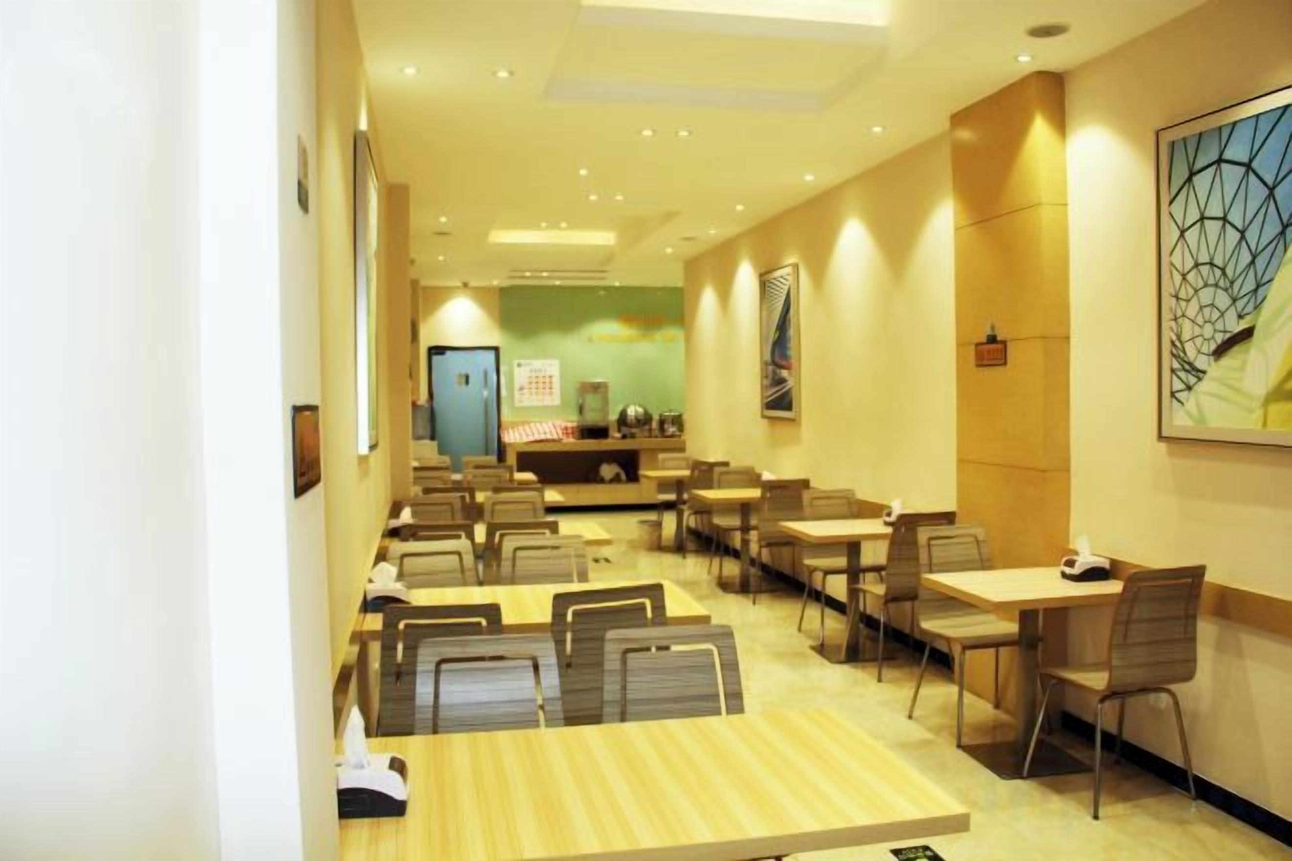 A hotel dining area with multiple tables and chairs, a reception desk, and artwork on the walls.