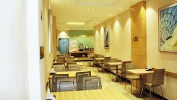 A hotel dining area with multiple tables and chairs, a reception desk, and artwork on the walls.
