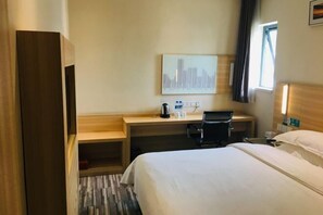 Une chambre d’hôtel avec un lit, un bureau et une chaise, une machine à café et un tableau représentant un paysage urbain accroché au mur.
