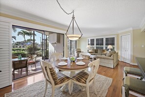 A dining area with a round table, chairs, and a hanging light fixture. - Rare Garden Unit | Pool, Grills & Beach Access (Marco Island)