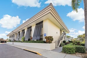 A building with a flat roof, multiple windows with shutters, a visible parking area, and a clear sky. - Rare Garden Unit | Pool, Grills & Beach Access (Marco Island)