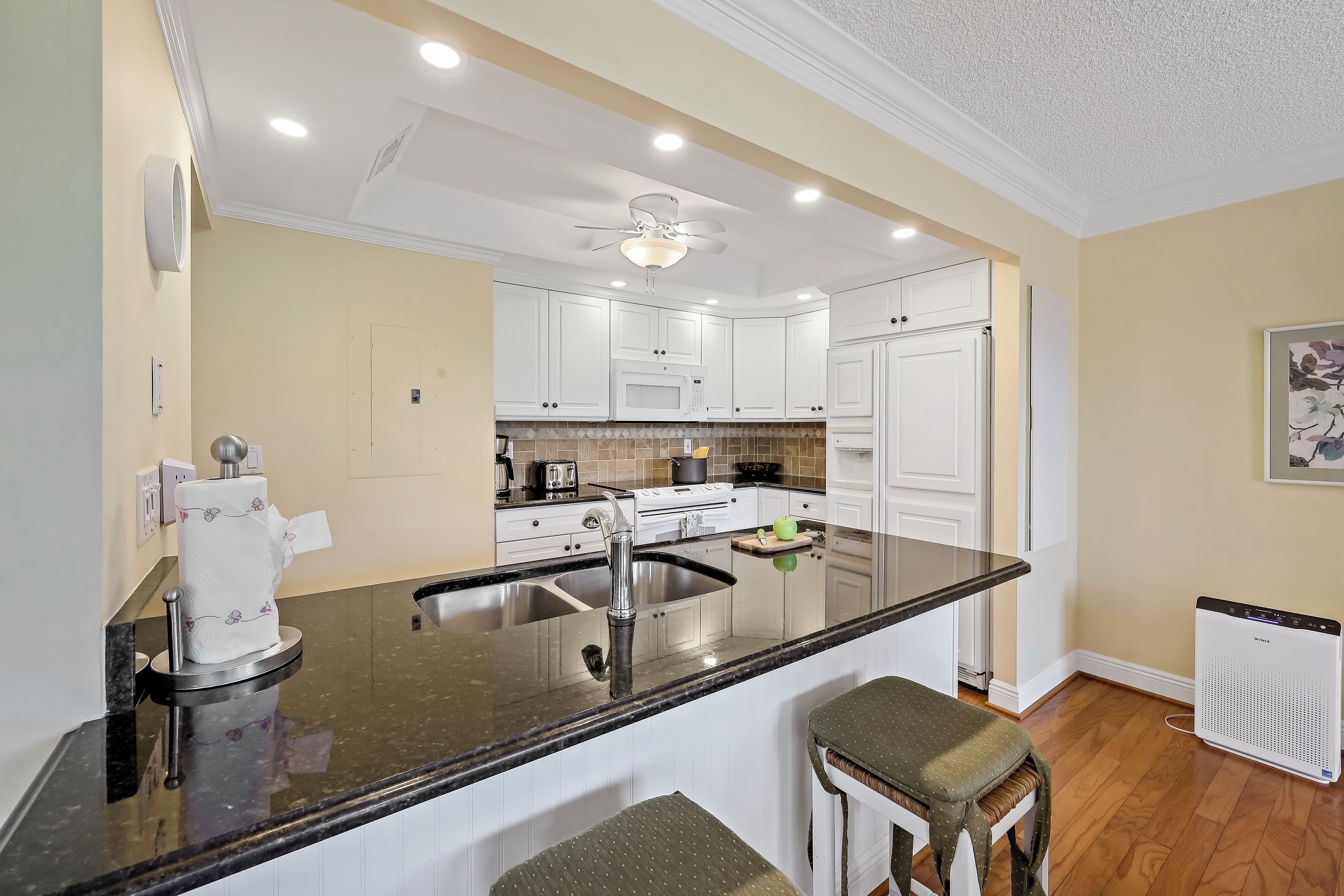 A kitchen with white cabinets, a black countertop, and a ceiling fan.