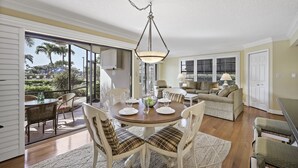 A dining area with a round table, chairs, and a hanging light fixture. - Rare Garden Unit | Pool, Grills & Beach Access (Marco Island)