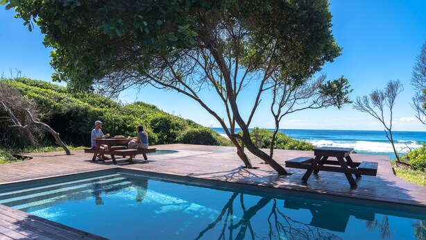 A pool area with wooden deck, picnic tables, and a view of the ocean. - Ponta Membene (Ponta Milibangalala)
