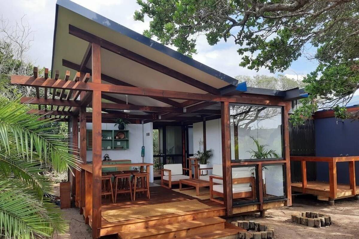 Eine Holzterrasse mit Gartenmöbeln, einer Pergola und Blick ins Innere.
