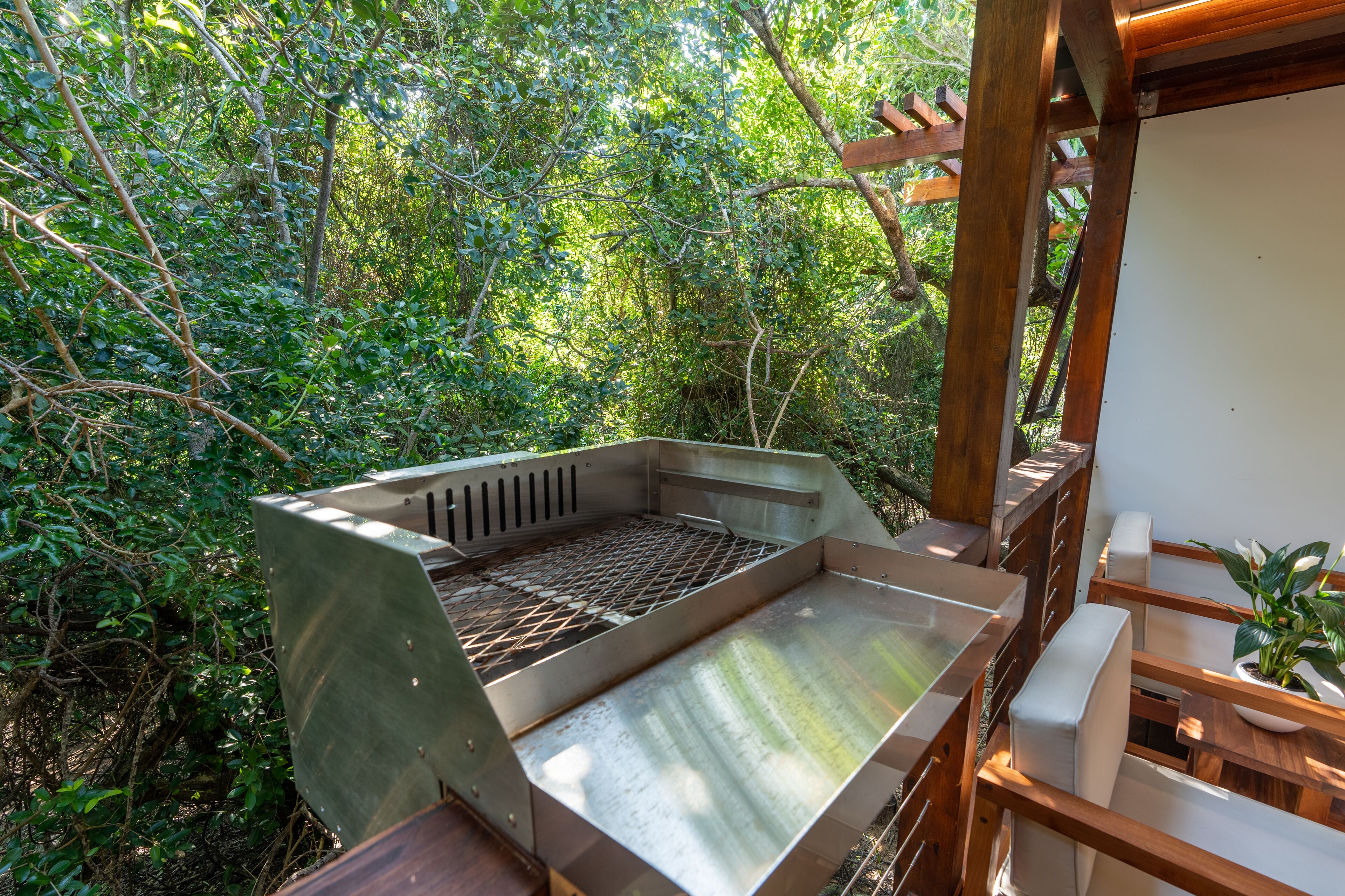 Un espace barbecue extérieur doté d’une grille en métal, entouré de meubles en bois et agrémenté d’une plante en pot.