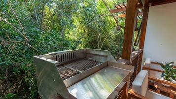 Un espace barbecue extérieur doté d’une grille en métal, entouré de meubles en bois et agrémenté d’une plante en pot.