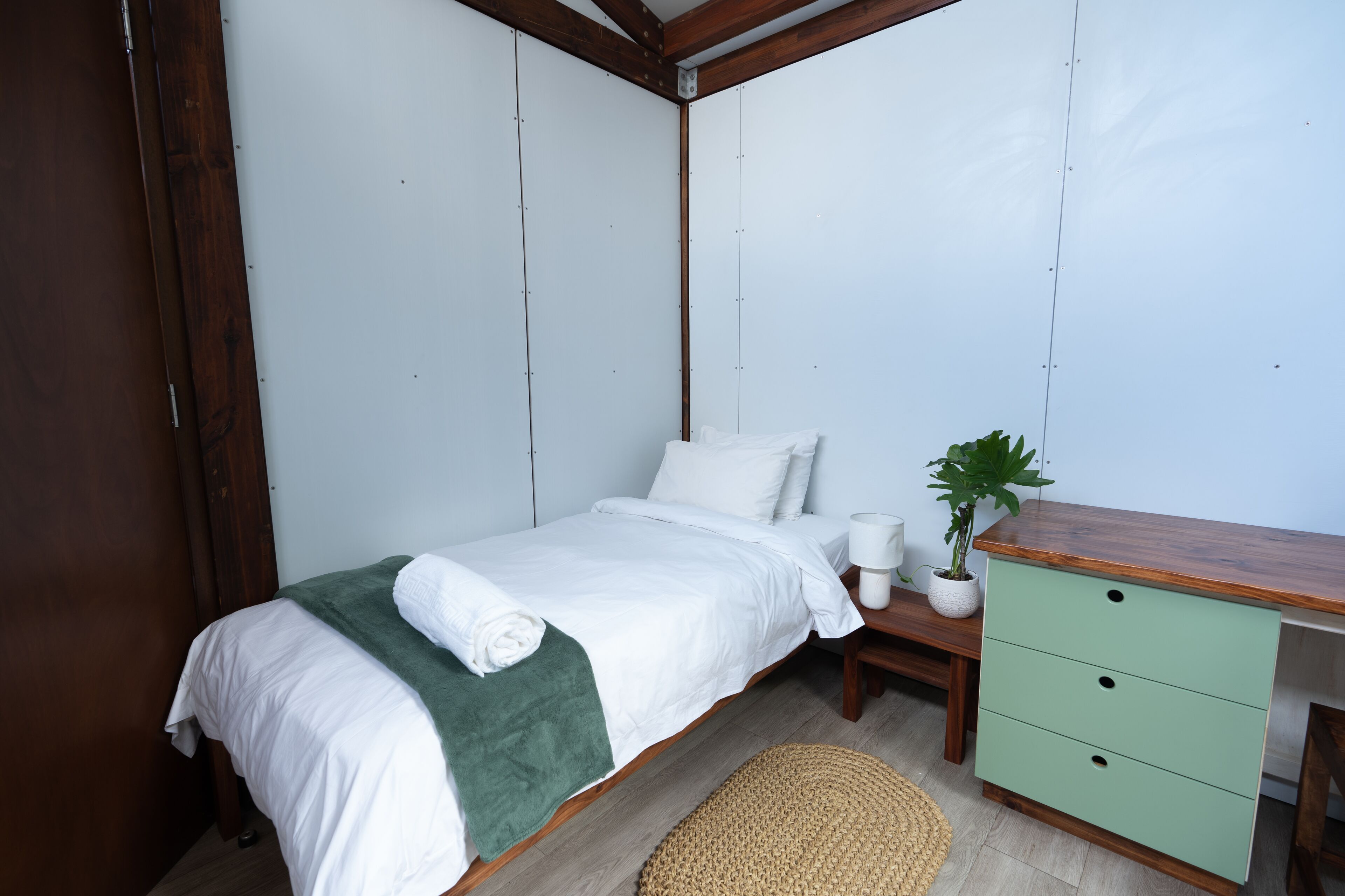 A bedroom with a bed, bedside table, green dresser, and a potted plant.